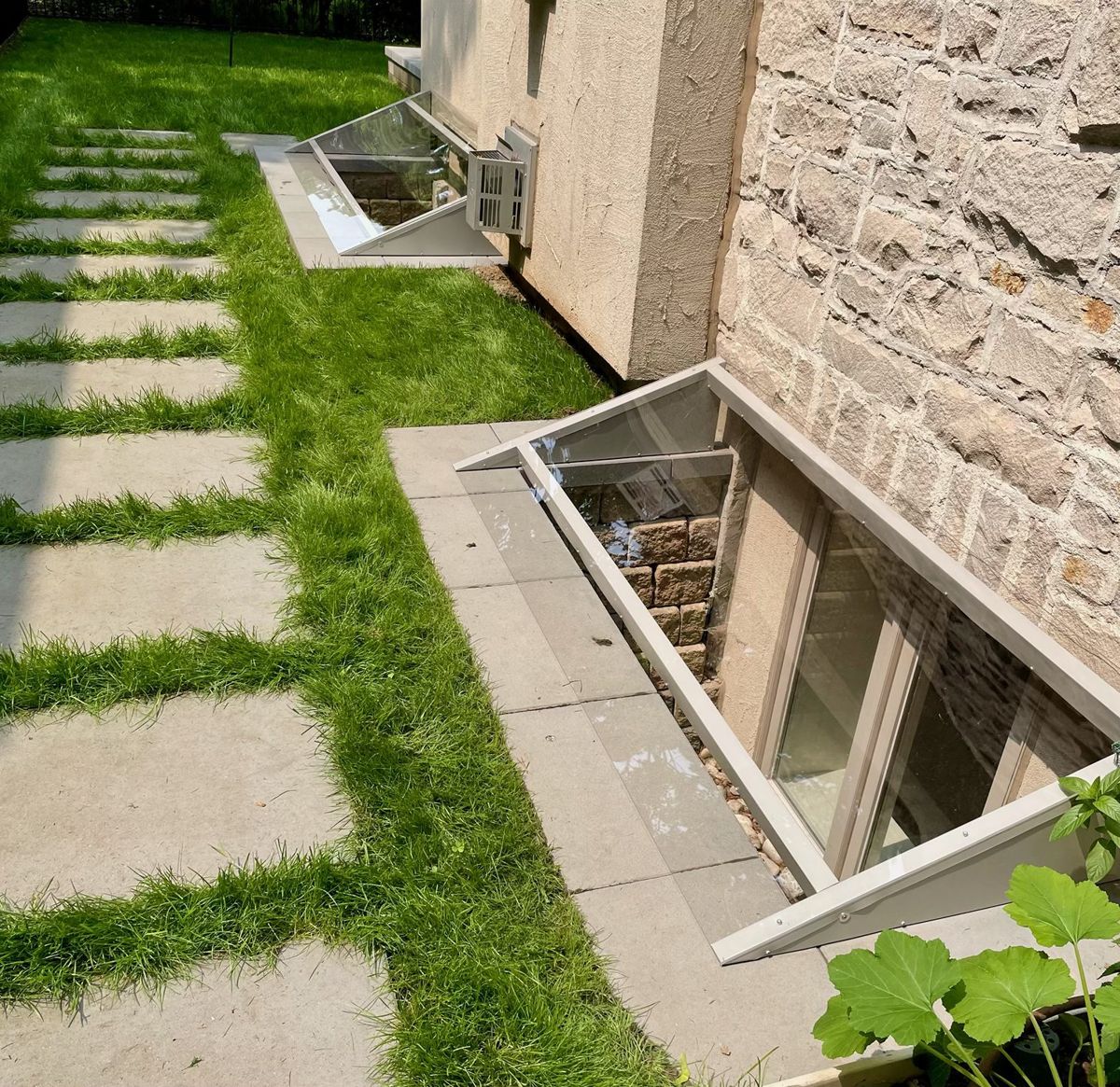Two clear custom window well covers along the side of a stone house